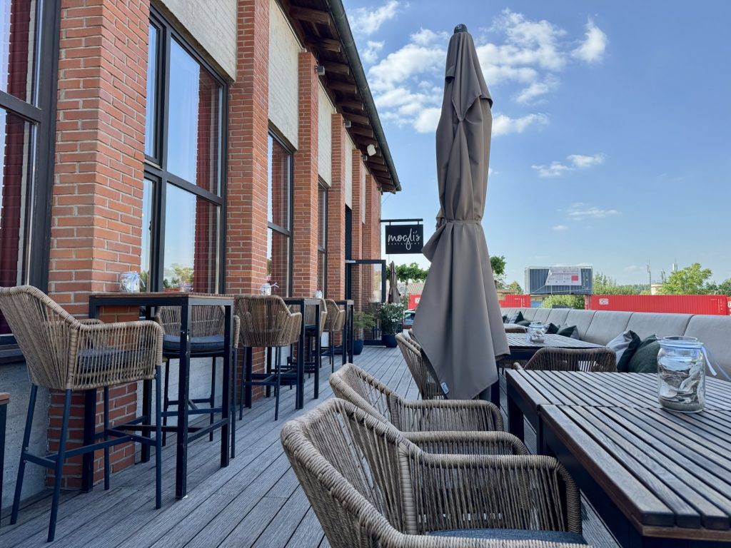Außenbereich des mogli’s Restaurants mit Rattanmöbeln und Sonnenschirmen auf Holzterrasse
