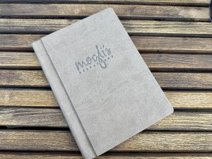 Nahaufnahme einer grauen Speisekarte mit mogli’s-Logo auf einem Holztisch